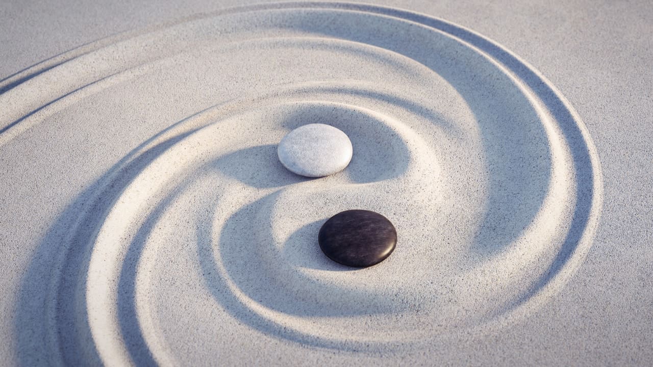 Yin und Yang symbolisiert in den Sand gezeichent, Ein Schwarzer und ein weißer Stein liegen in der Mitte
